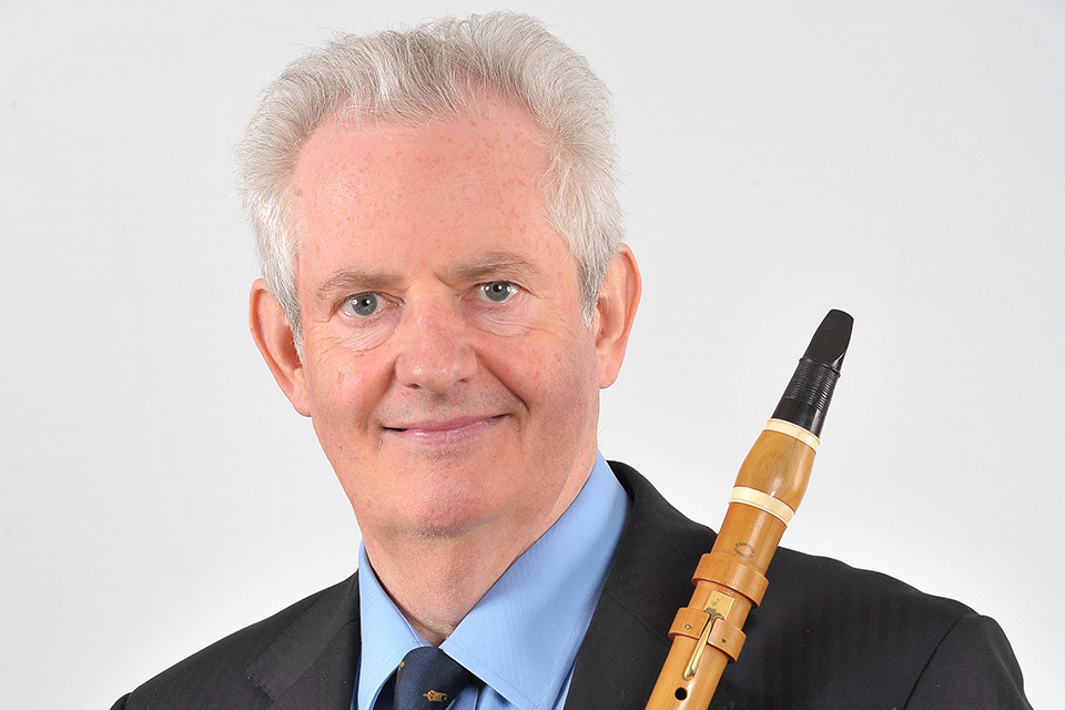 A man, smiling at the camera, wearing a suit and holding a clarinet.